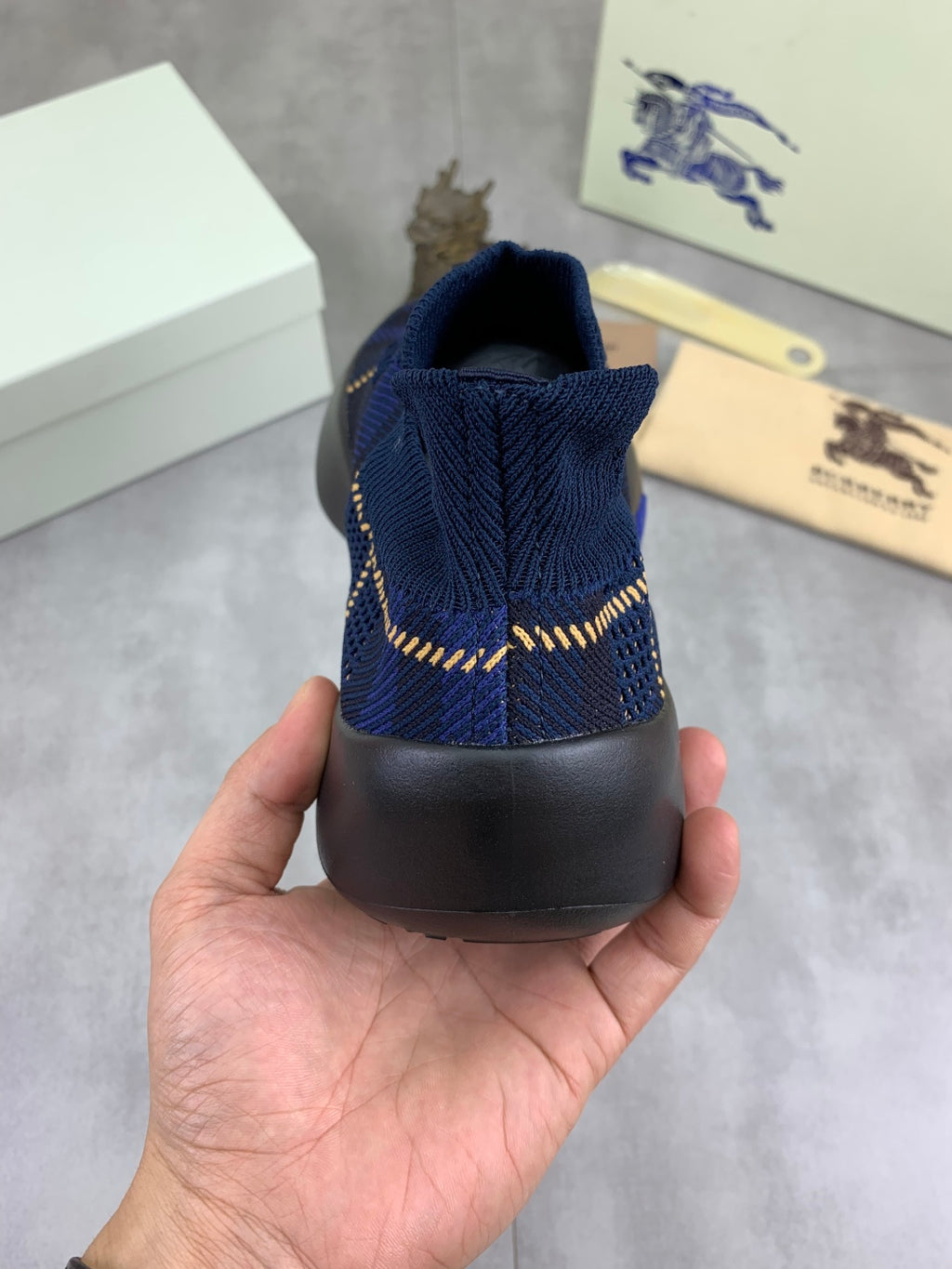 Burberry blue knit sneaker heel view with black rubber sole and gold trim detail