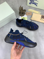 Burberry blue knit sneakers held in hand, black soles with blue accents and gold trim