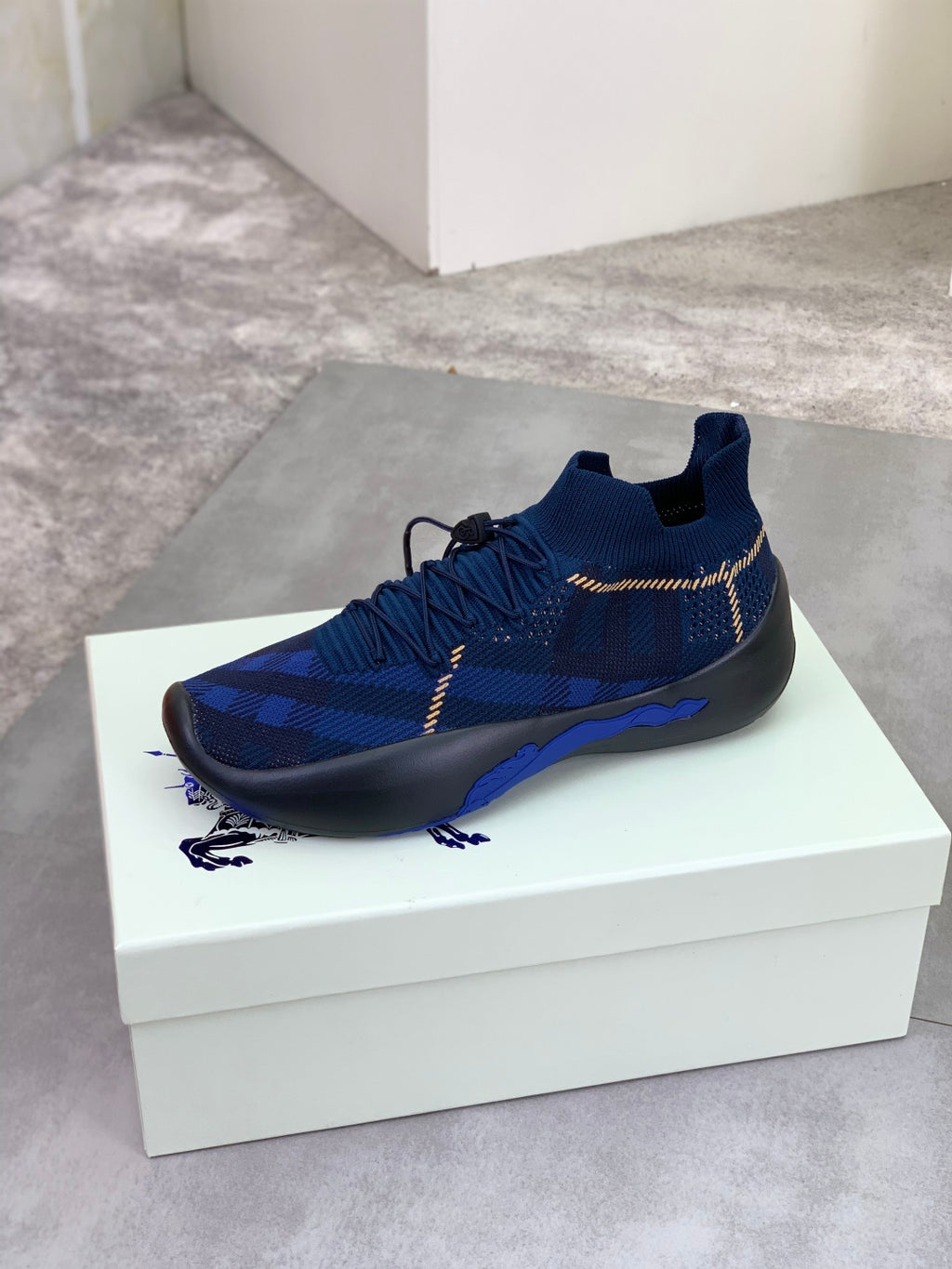 Burberry blue knit sneaker on white box, black outsole and gold trim laces