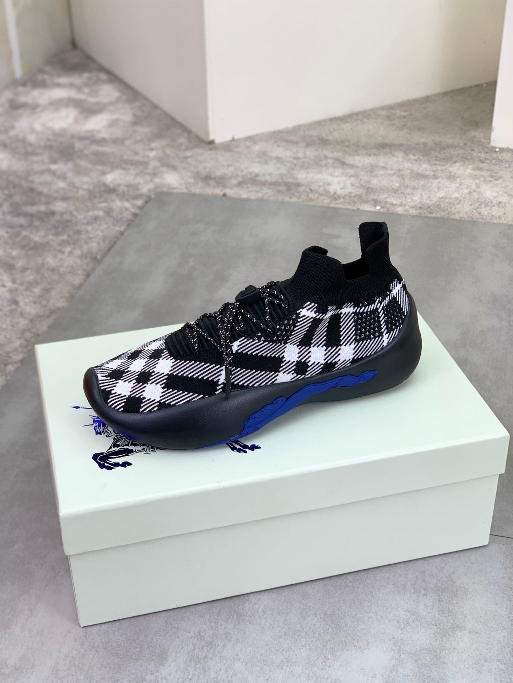 Black and white check knit sneaker on box, rounded toe and blue sole