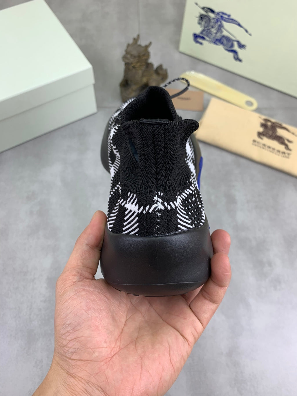 Rear view of black and white check knit sneaker with elastic heel and blue sole