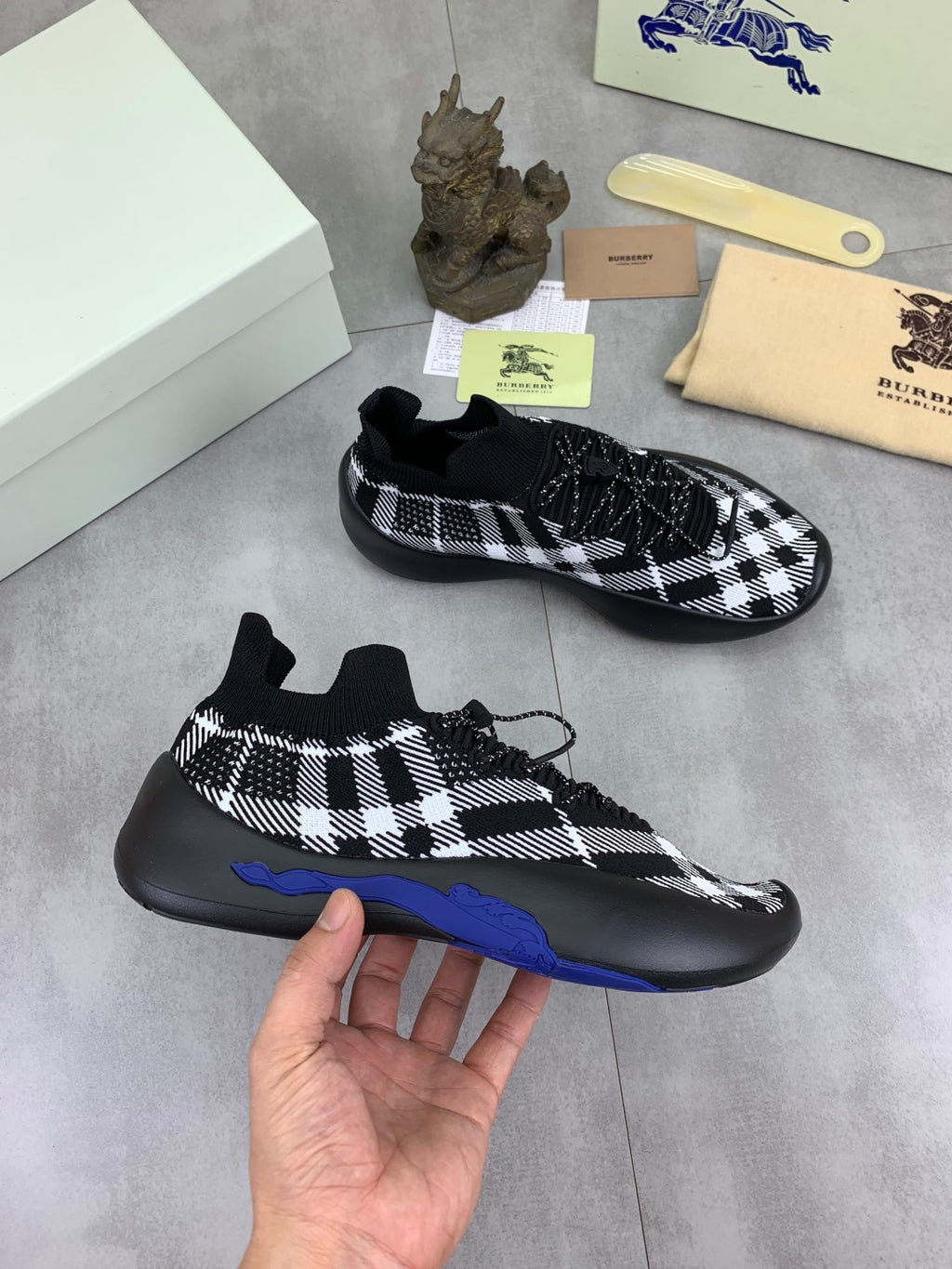 Black and white check knit sneaker pair, one held in hand showing blue sole edge