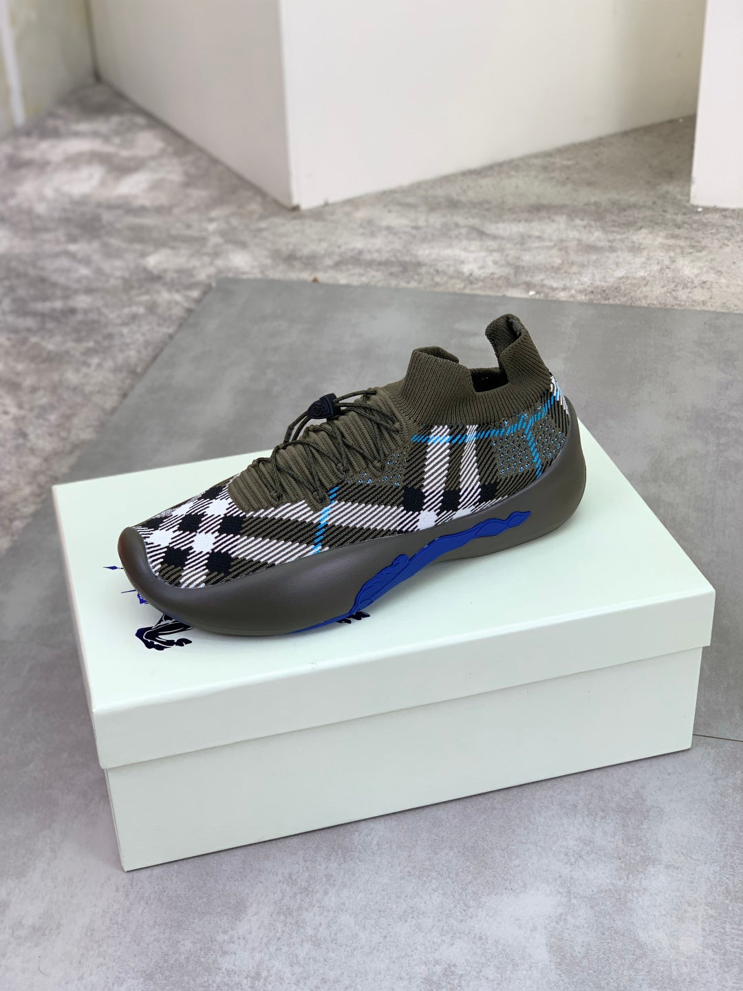 Burberry knit sneakers on white box, dark olive with check pattern and blue sole edge