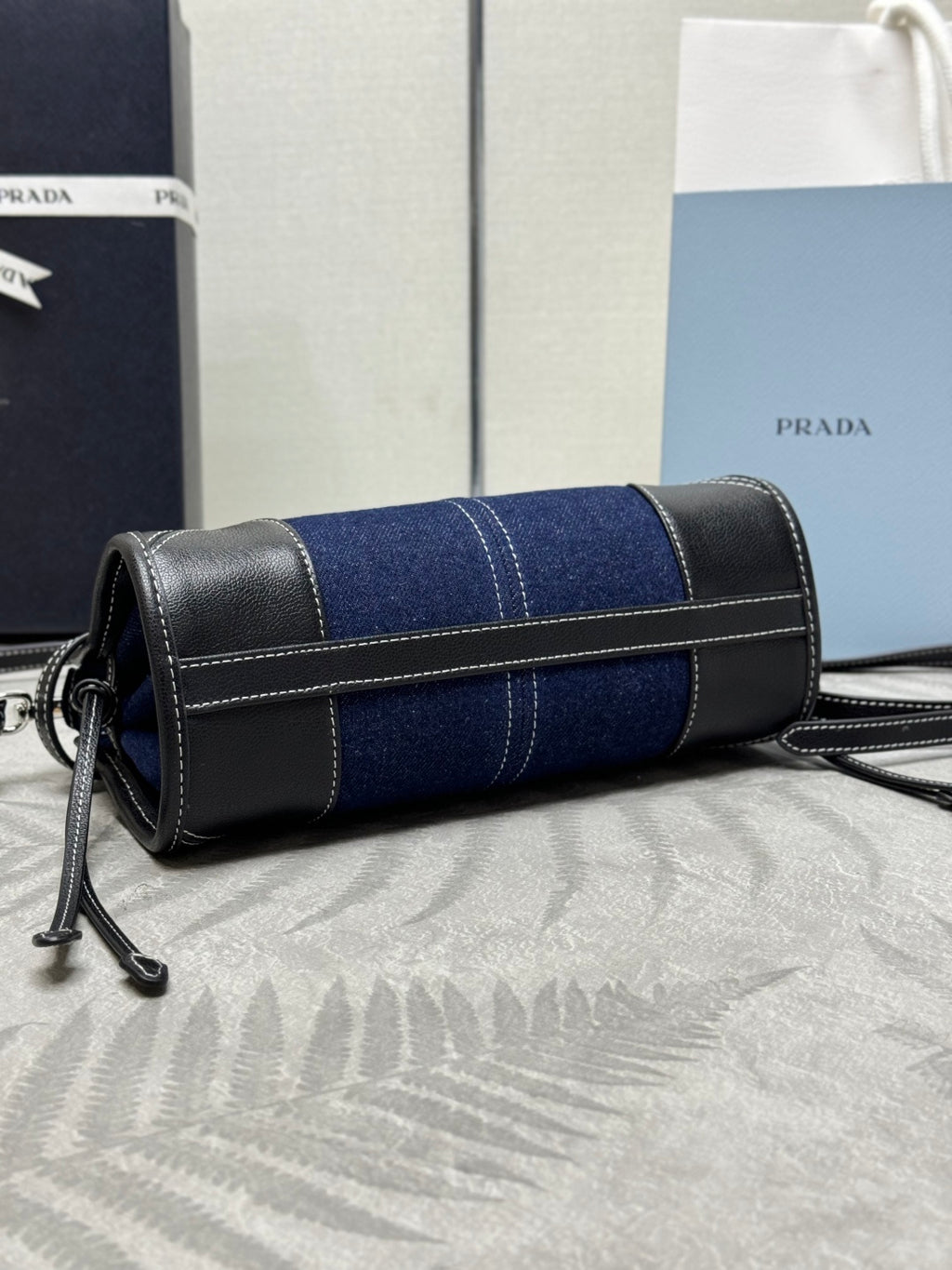 Prada cylindrical crossbody bag in navy denim with black leather trim and adjustable strap