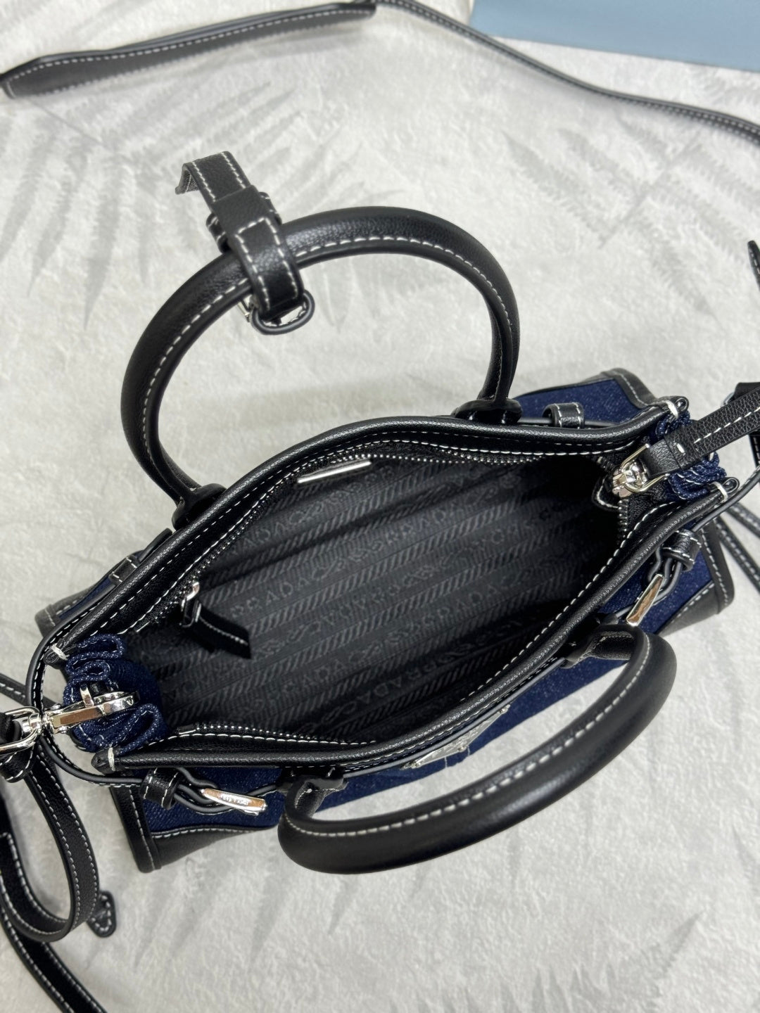 Prada mini bag open view with black zipper lining, dark blue exterior, crossbody strap