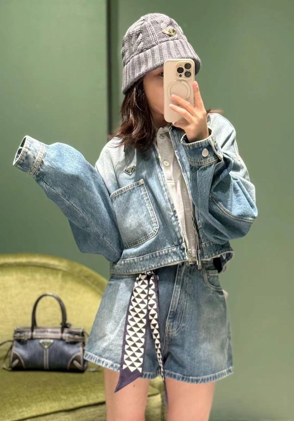 Denim Prada bag with top handle and front triangle logo, partially visible behind person