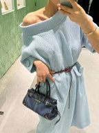 Denim handbag with top handle and front triangle logo, shown on a person