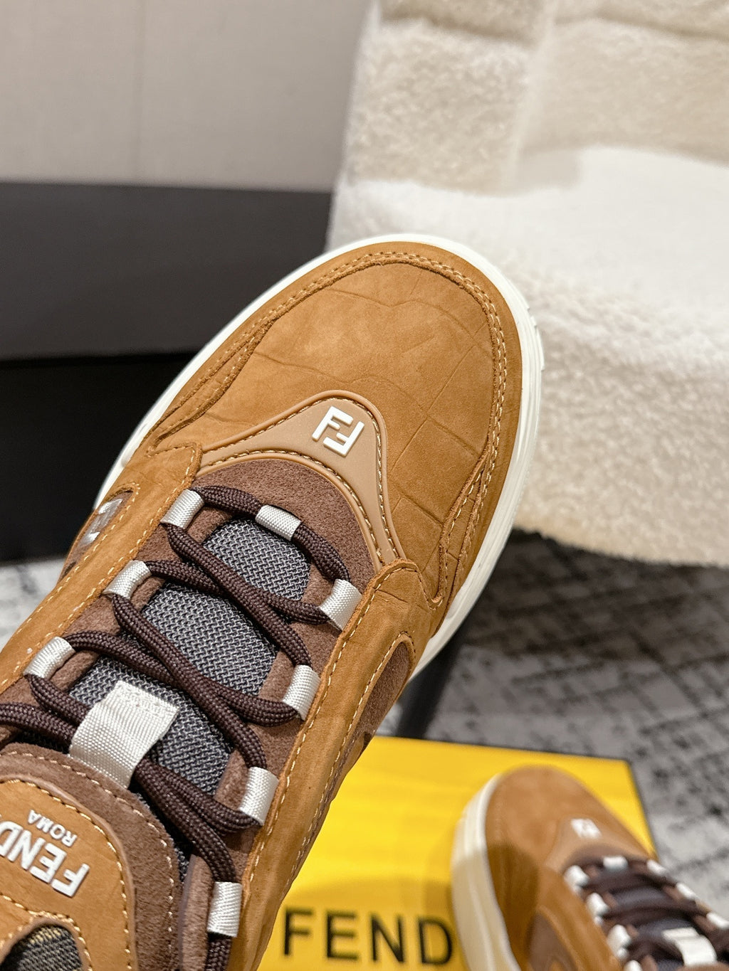 Fendi unisex sneaker close-up: tan suede upper, textured laces, logo patch on side