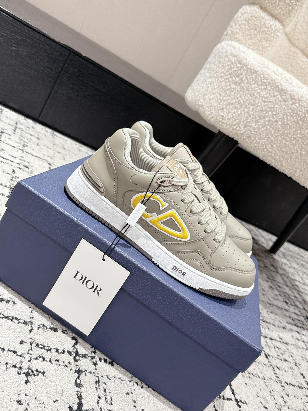 Beige Dior lace-up sneakers with side yellow logo, shown on blue box