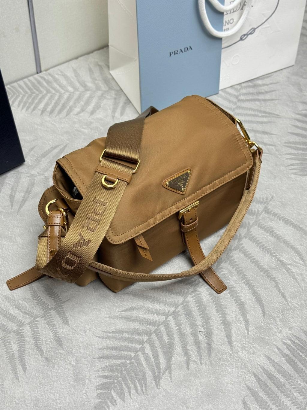Tan shoulder bag with flap and buckle strap, gold hardware, angled view