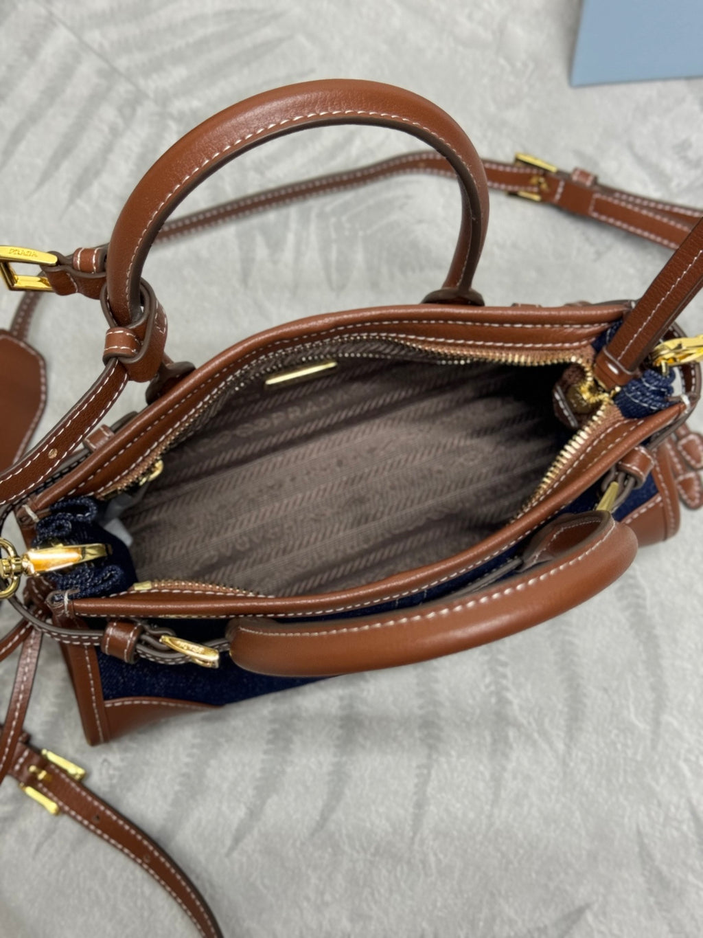 Prada denim and leather handbag open view with brown interior and gold zipper pulls