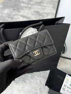 Small quilted flap bag in dark gray/black with front button and gold-tone logo.