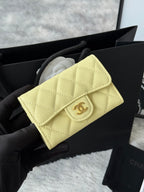 Small quilted flap bag in light yellow with gold-tone logo on front.