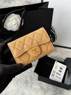 Small quilted flap wallet bag in tan with gold logo clasp, held in a hand.