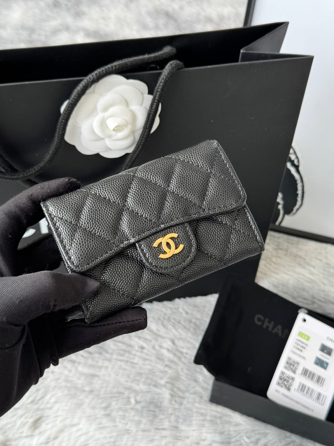 Small quilted flap bag in dark gray/black with gold-tone logo on front.