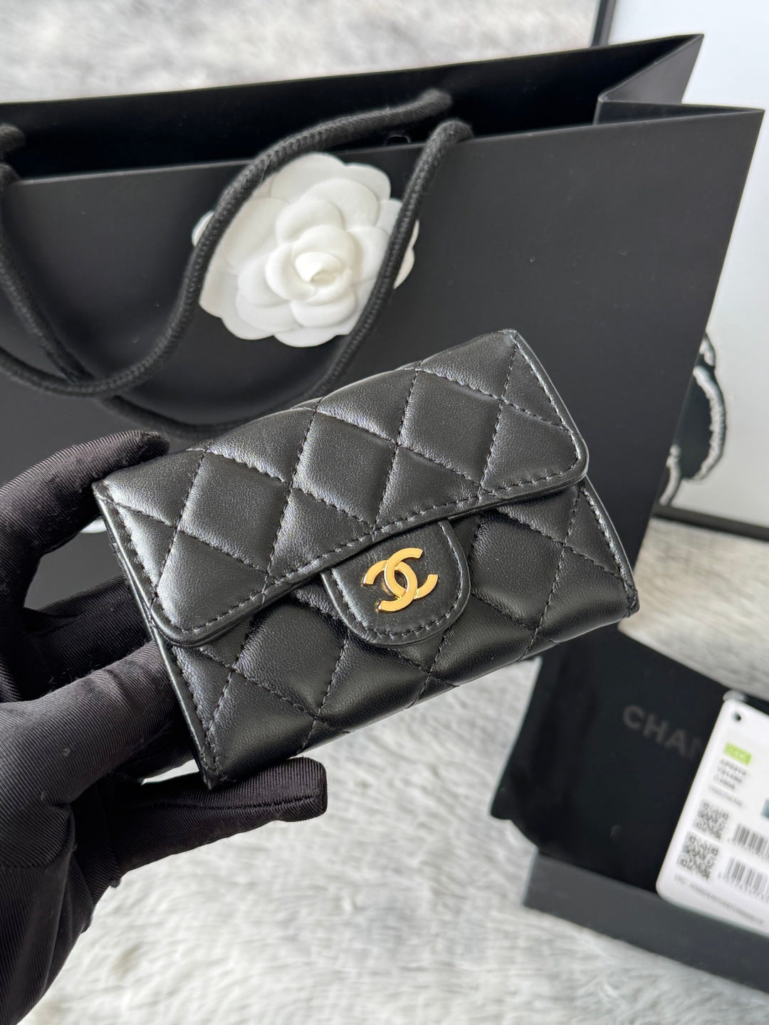 Small quilted flap bag in dark gray/black with gold-tone logo and structured top flap.