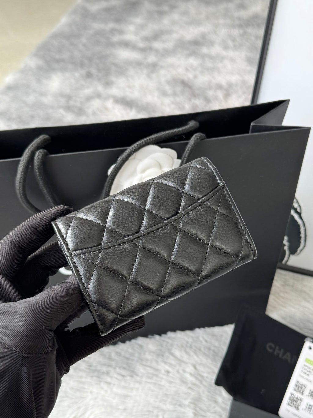 Small quilted flap bag in dark gray/black with angled front panel and gold-tone logo.