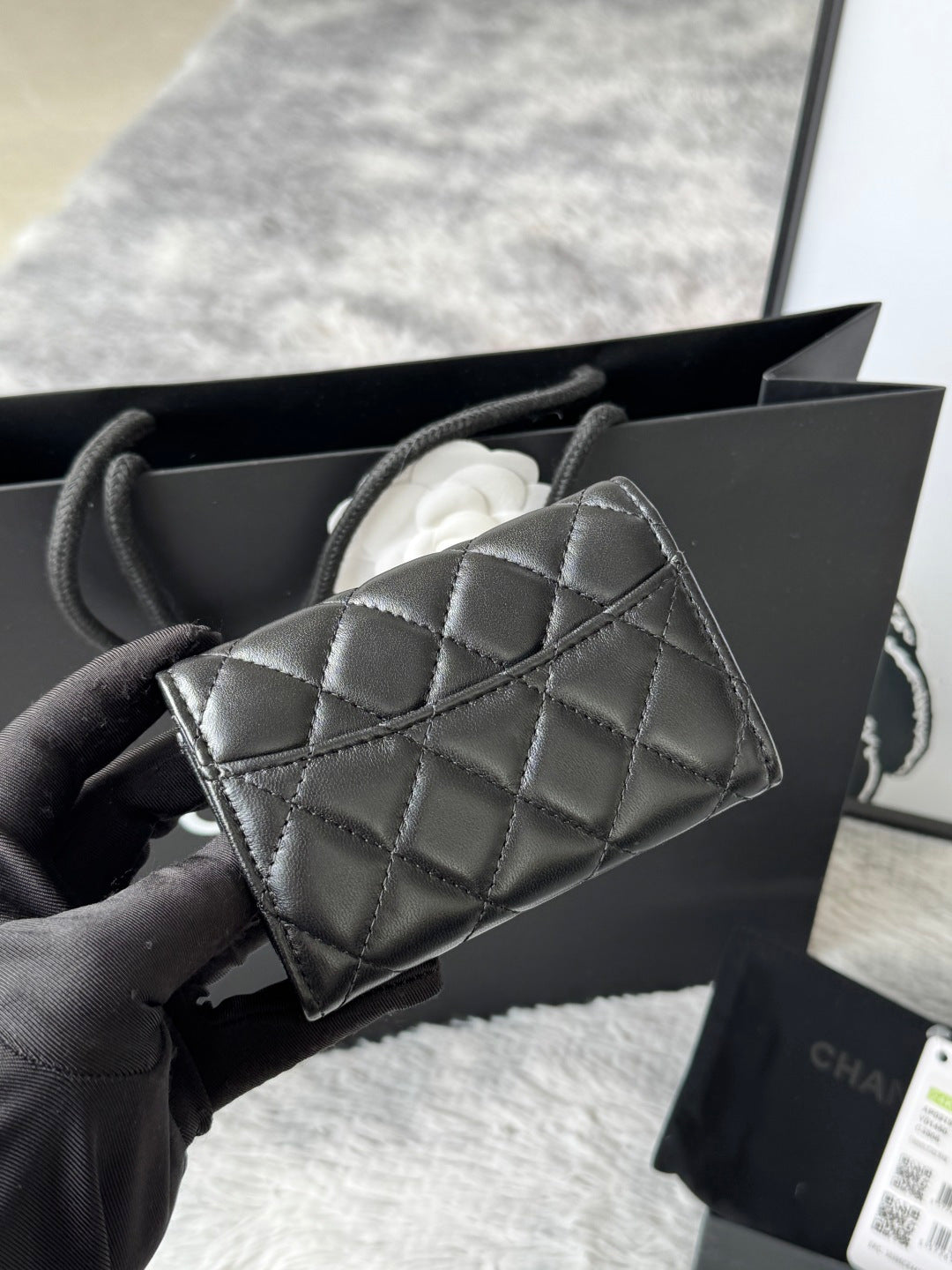 Small quilted flap bag in dark gray/black with angled front panel and gold-tone logo.