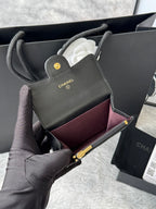 Small quilted flap bag in dark gray/black with gold-tone logo and burgundy interior.