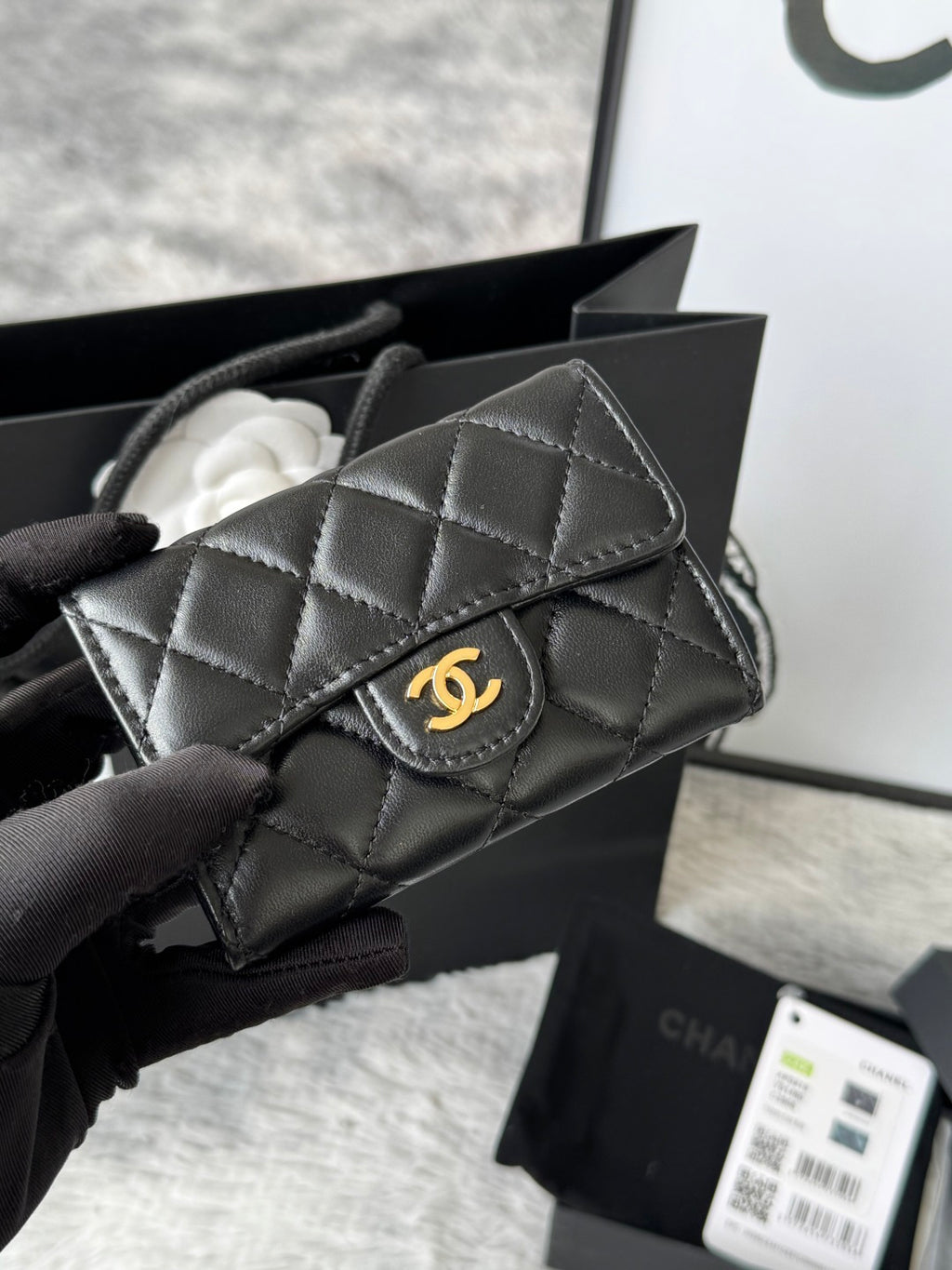 Small quilted flap bag in dark gray/black with stitched panels and gold-tone logo.