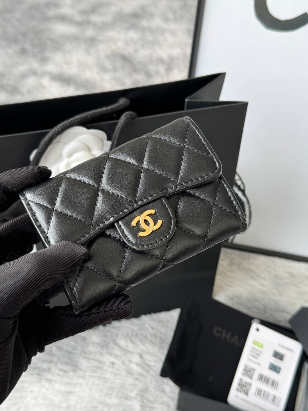 Small quilted flap bag in dark gray/black with stitched panels and gold-tone logo.