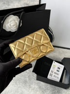 Small quilted flap wallet bag in shiny gold with gold logo clasp, held in a hand.