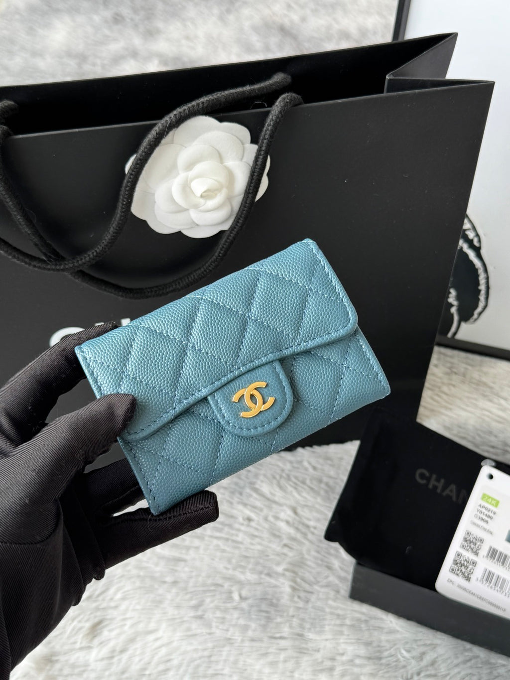 Quilted flap bag with gold logo, light blue textured leather, magnetic snap closure.