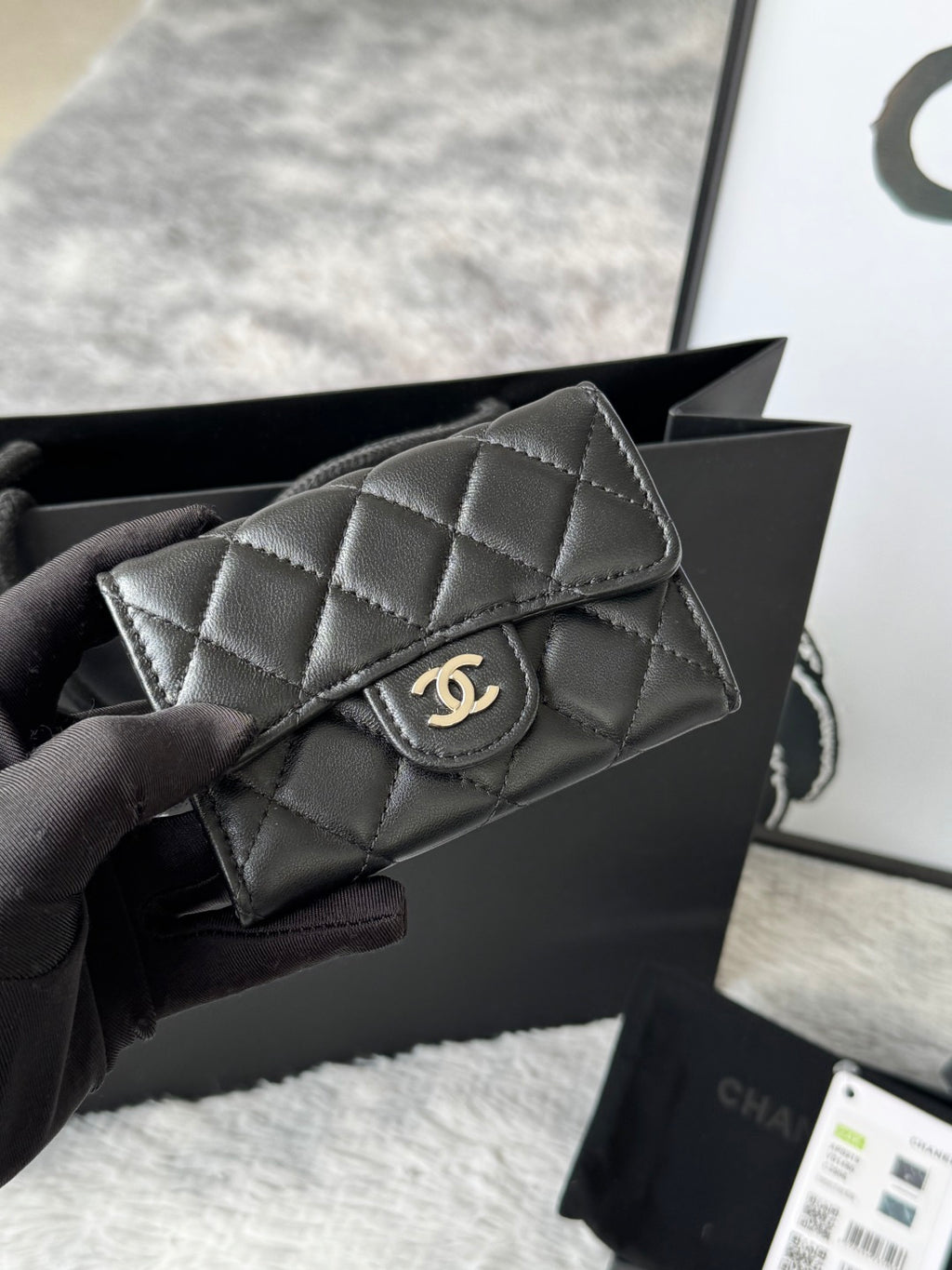 Small quilted flap bag in dark gray/black with gold-tone CC-style logo on front.