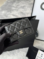 Small quilted flap bag in dark gray/black with gold-tone CC-style logo on front.