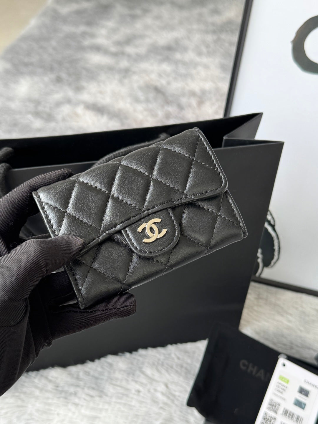 Small quilted flap bag in dark gray/black with gold-tone CC-style logo on front.