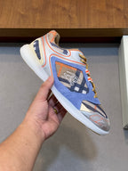 Burberry blue sneakers held in hand, with orange trims, patterned upper, lace-up