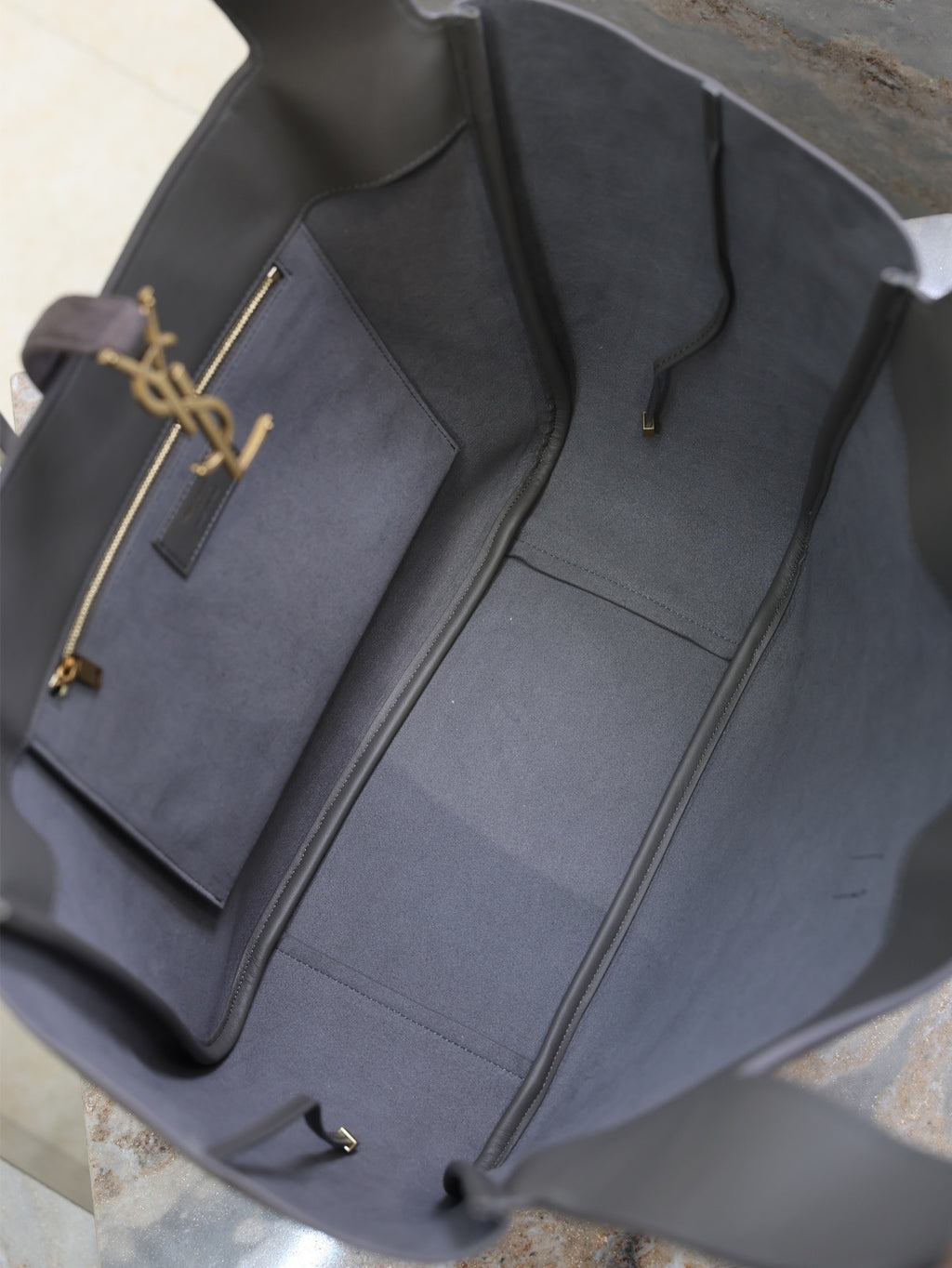 Dark gray tote bag interior with open top, light lining, and YSL logo charm