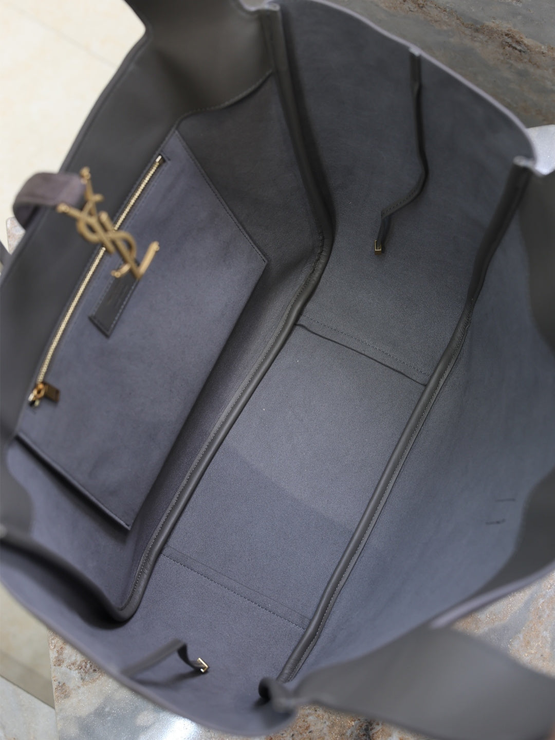 Dark gray tote bag interior with open top, light lining, and YSL logo charm
