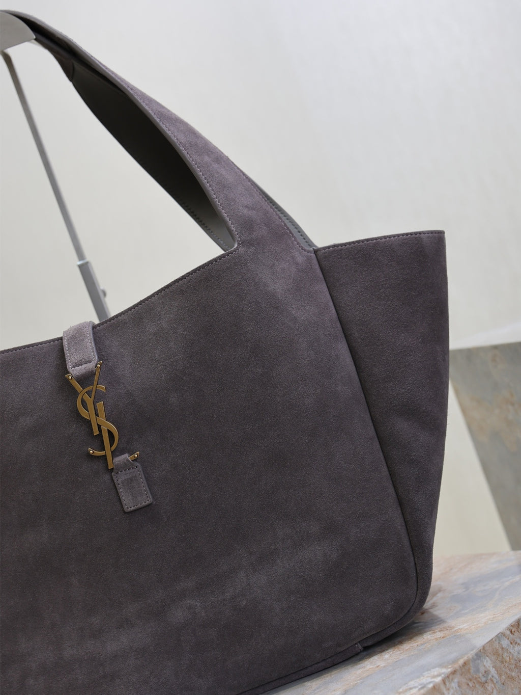Dark gray suede tote bag close-up of YSL logo charm on front strap