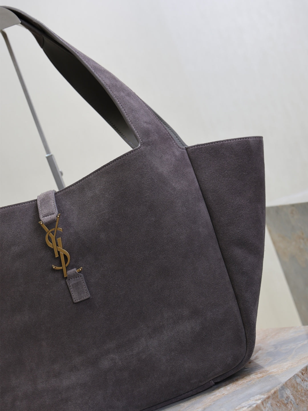 Dark gray suede tote bag close-up of YSL logo charm on front strap
