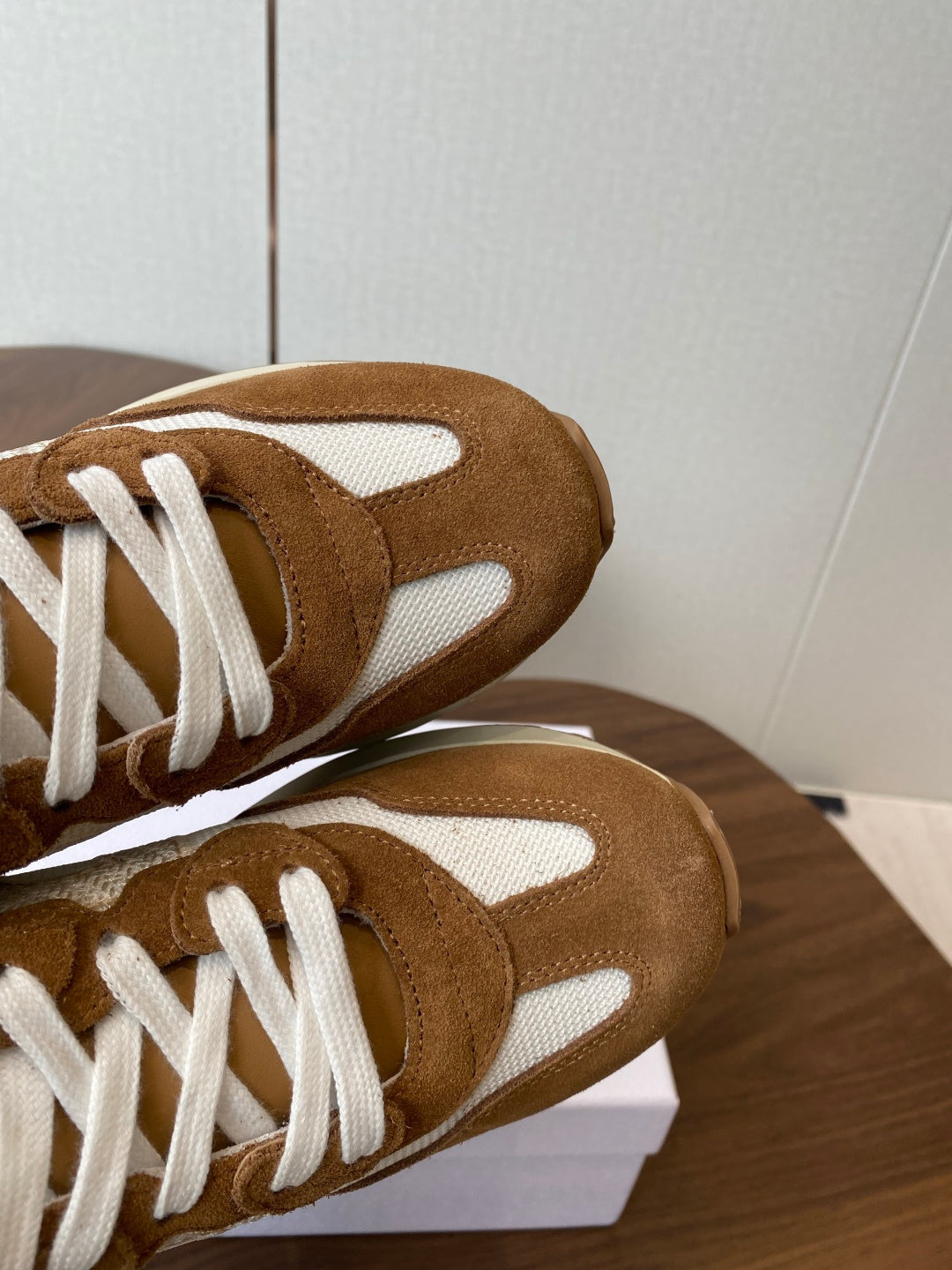 Close-up of brown suede sneaker toe and white laces, on white shoebox