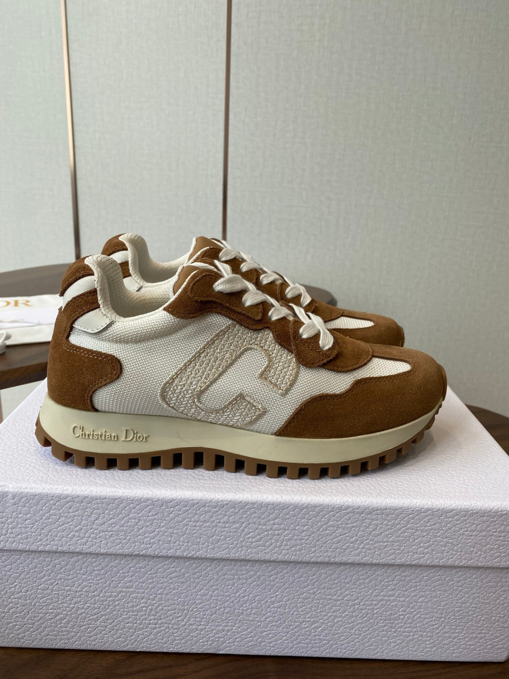 Brown and white Dior sneakers with white laces, side view on white shoebox