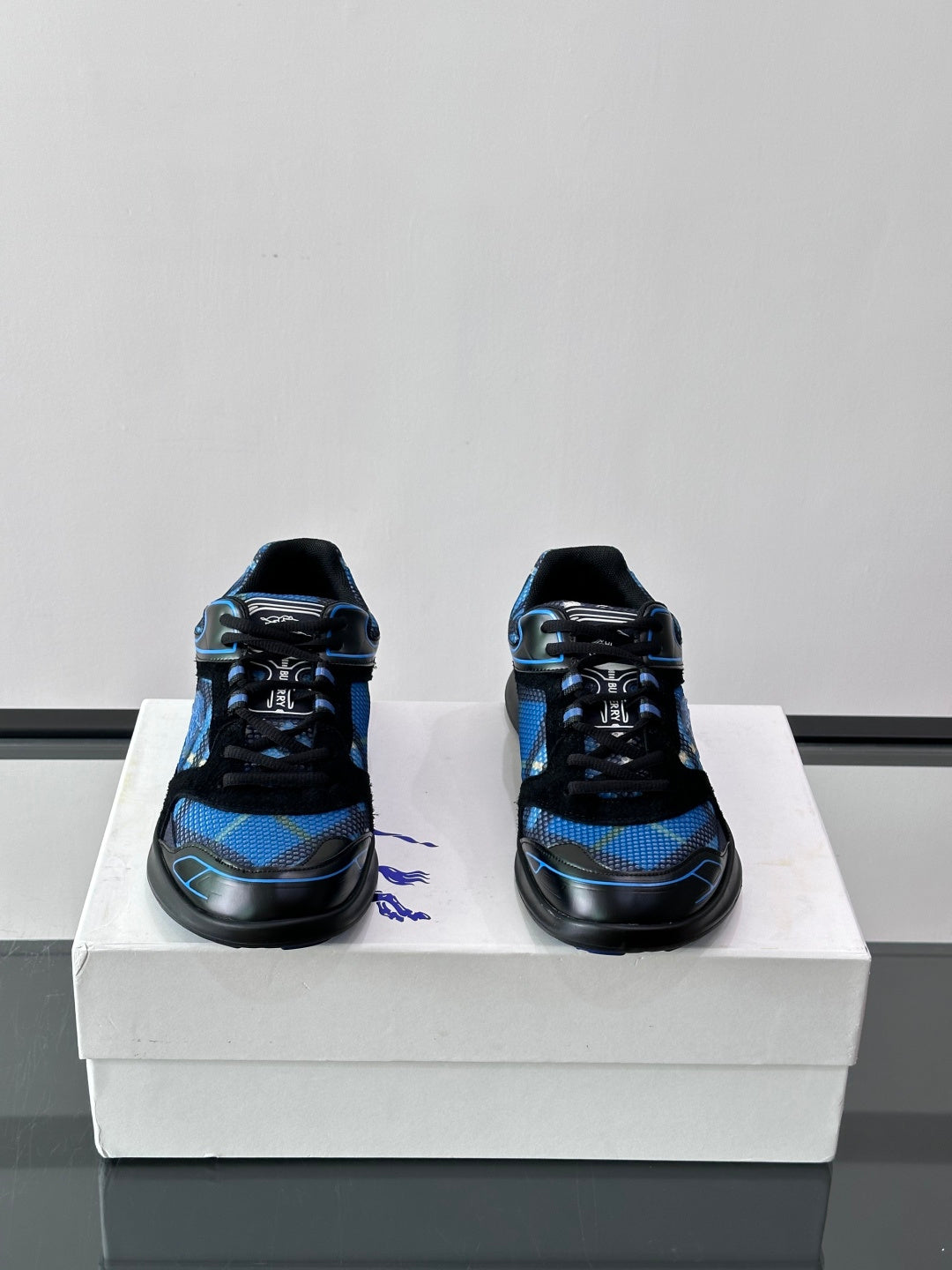 Pair of blue and black sneakers shown from the front on a white shoebox