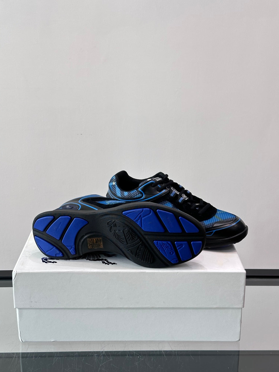 Blue and black sneakers with patterned outsole visible in a rear three-quarter view