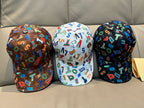 Three baseball caps with multicolor letter prints: black, white, and dark patterned.