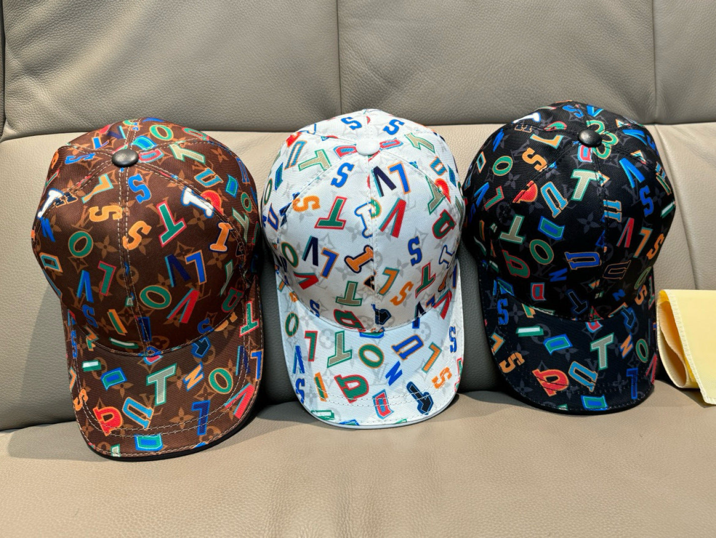 Three Louis Vuitton caps: brown, white, and dark with multicolor letter patterns