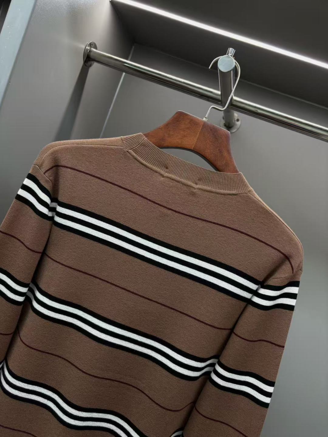 Brown striped knit sweater on hanger with black-and-white horizontal stripes