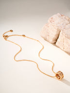 Gold-tone necklace with circular charm at end and chain draped on light stone