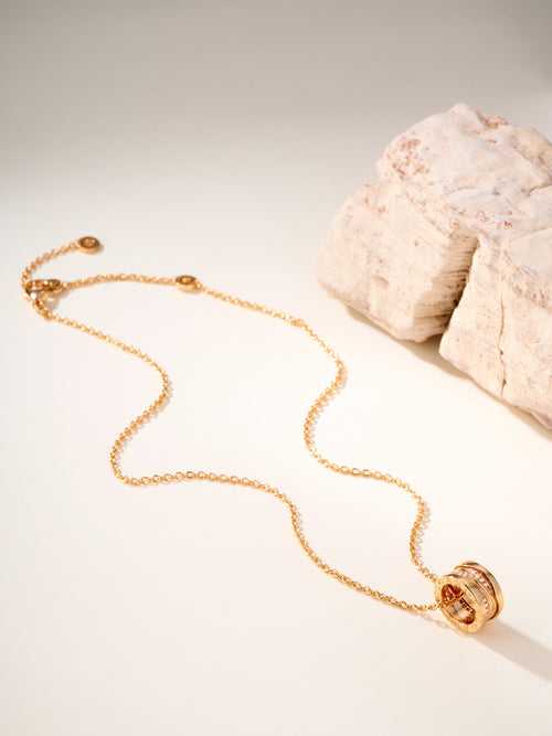 Gold-tone necklace with circular charm at end and chain draped on light stone