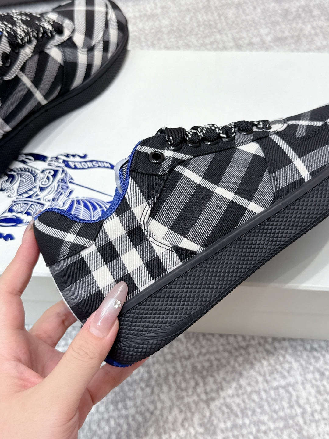 Close-up of check-pattern sneaker lace-up with blue logo patch at tongue