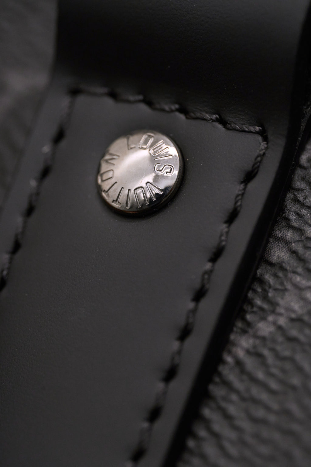 Round logo snap button on dark leather trim of monogram handbag