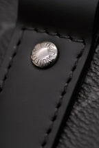 Round logo snap button on dark leather trim of monogram handbag