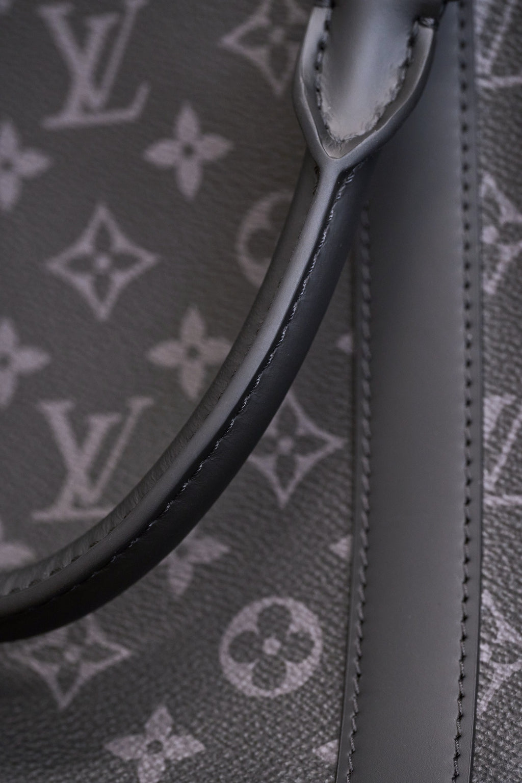 Handle strap attachment and curved top edge on dark monogram canvas handbag