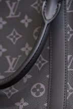 Handle strap attachment and curved top edge on dark monogram canvas handbag