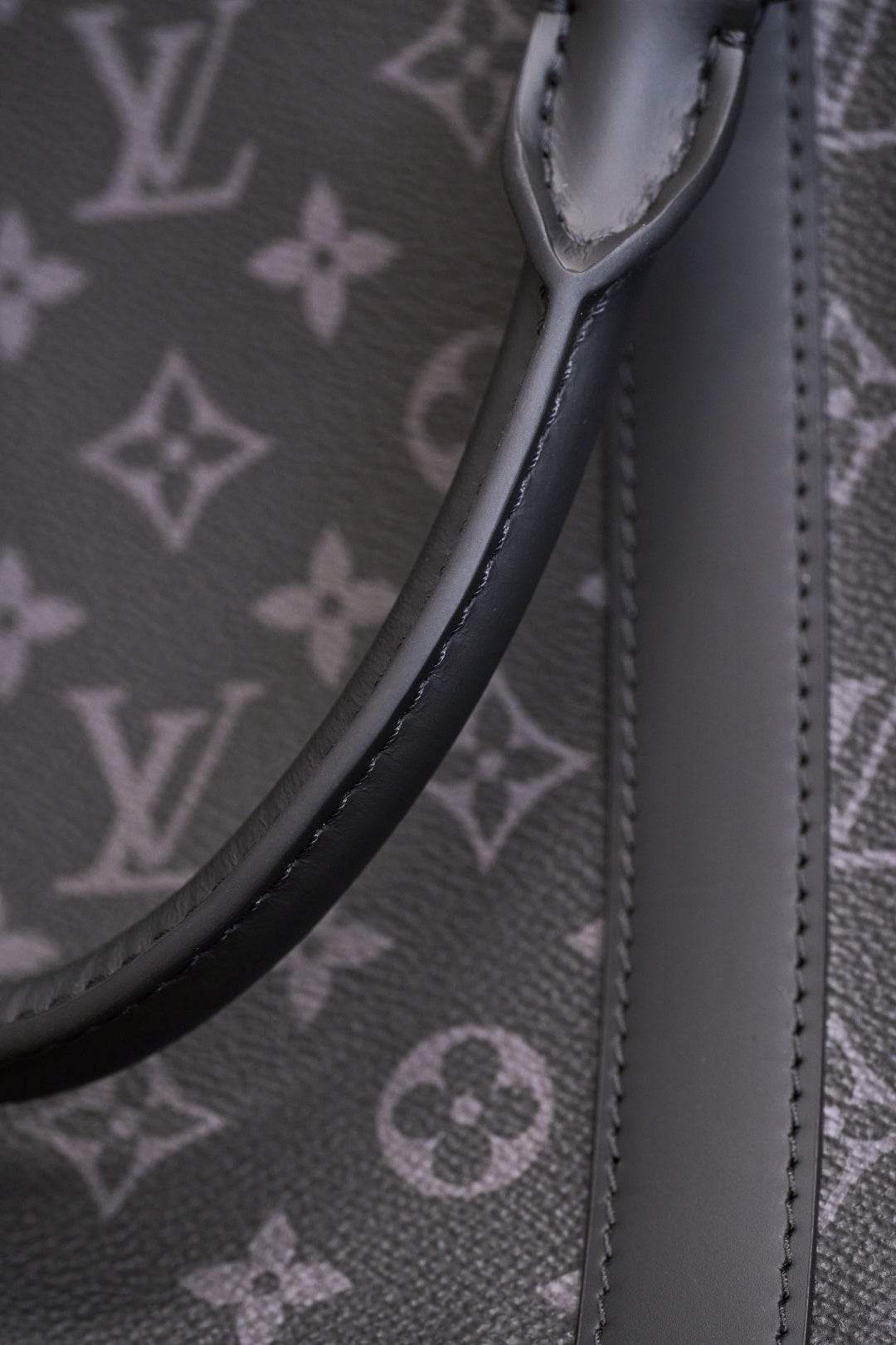 Handle strap attachment and curved top edge on dark monogram canvas handbag